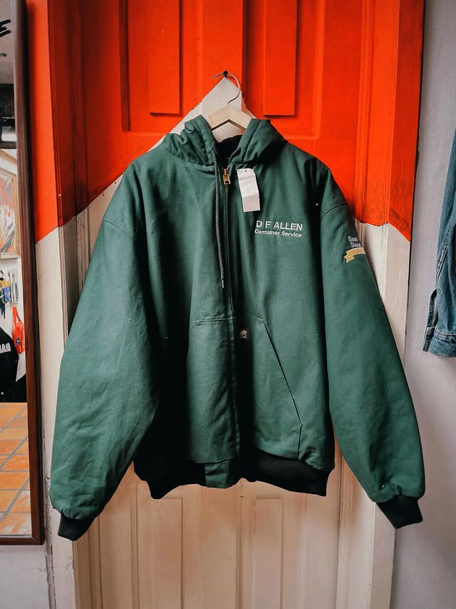 Chamarra de trabajo verde colgada en puerta naranja