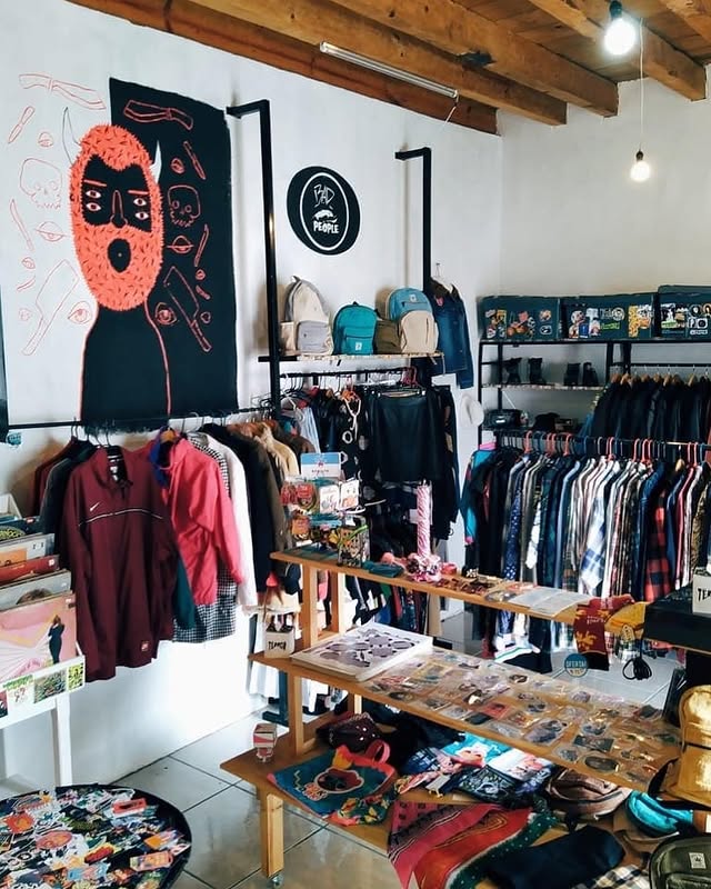 Interior de la tienda Bad People, racks de ropa y mural en la pared